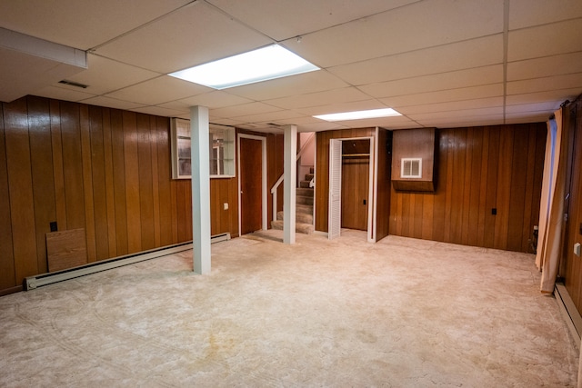 basement featuring a drop ceiling, baseboard heating, and wooden walls