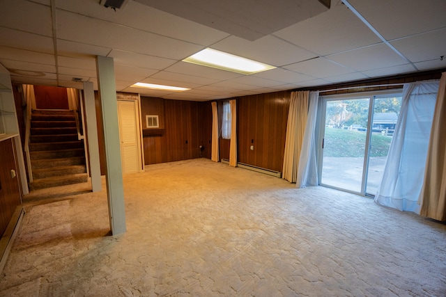 basement with a baseboard radiator, a drop ceiling, light colored carpet, and wooden walls