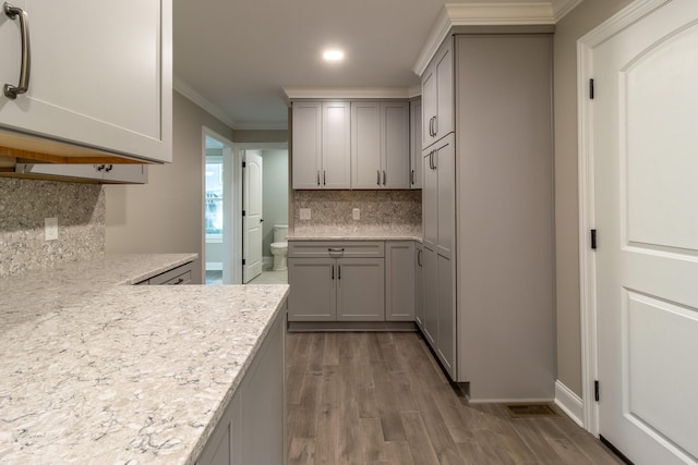 kitchen featuring backsplash, ornamental molding, gray cabinets, light stone counters, and dark hardwood / wood-style flooring