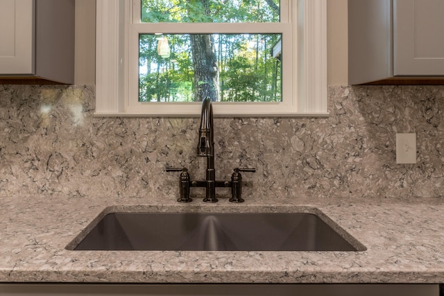 room details with sink, light stone countertops, white cabinetry, and tasteful backsplash