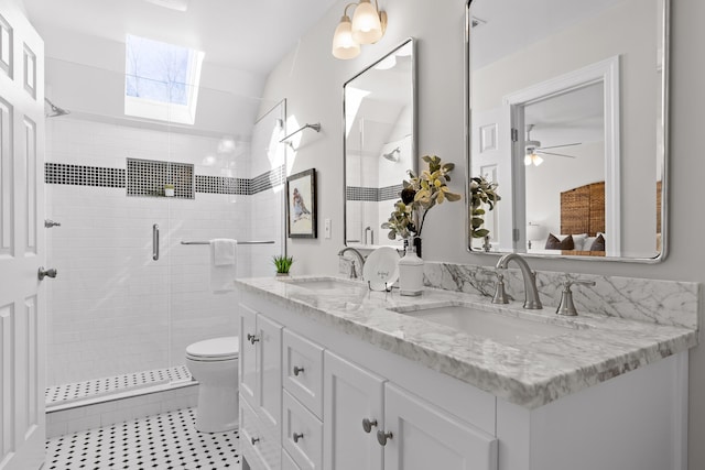 bathroom featuring a skylight, ceiling fan, toilet, vanity, and a shower with shower door