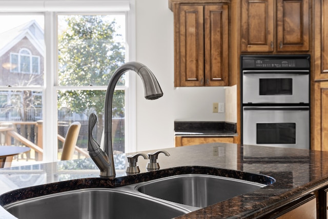 kitchen featuring double oven, dark stone countertops, and sink