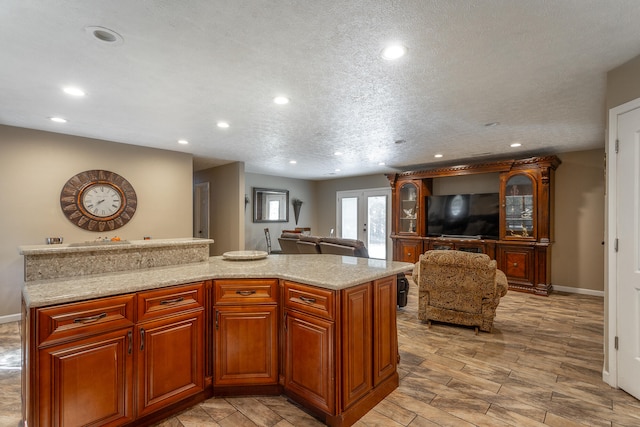 kitchen featuring french doors, light stone counters, a kitchen island, a textured ceiling, and light hardwood / wood-style flooring