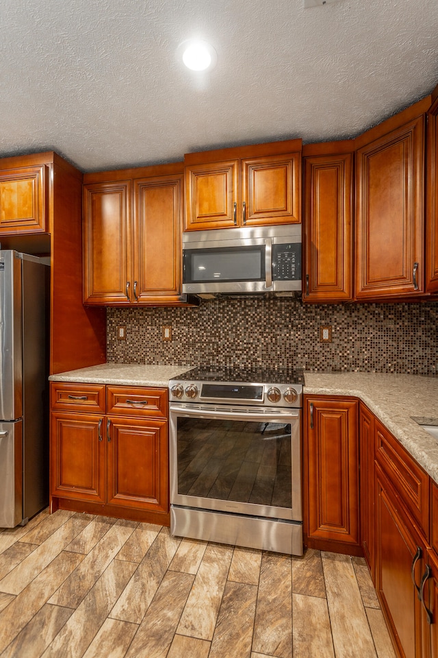 kitchen featuring decorative backsplash, stainless steel appliances, a textured ceiling, and light stone countertops