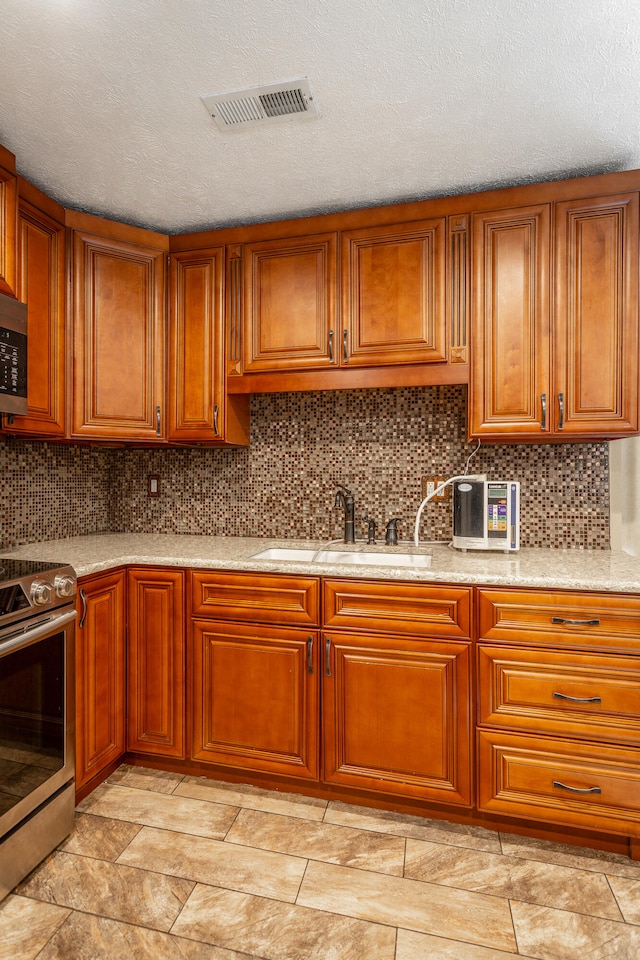 kitchen featuring a textured ceiling, sink, tasteful backsplash, stainless steel stove, and light stone countertops