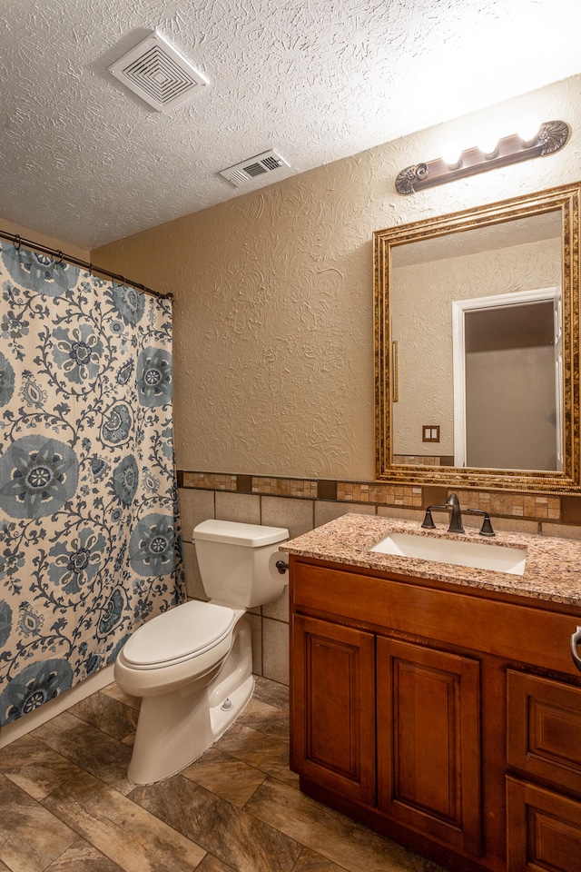 bathroom featuring toilet, vanity, a textured ceiling, and tile walls