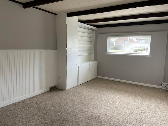 empty room with wood walls, beamed ceiling, and carpet floors