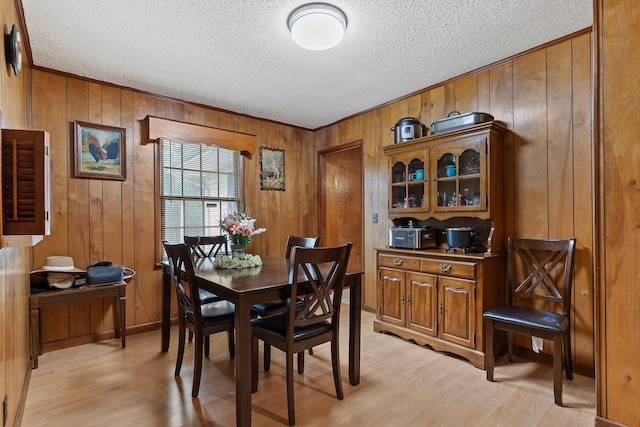 dining room featuring wood walls, a textured ceiling, and light hardwood / wood-style floors