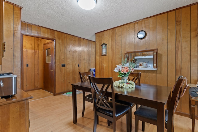 dining space with wood walls, light hardwood / wood-style floors, and a textured ceiling