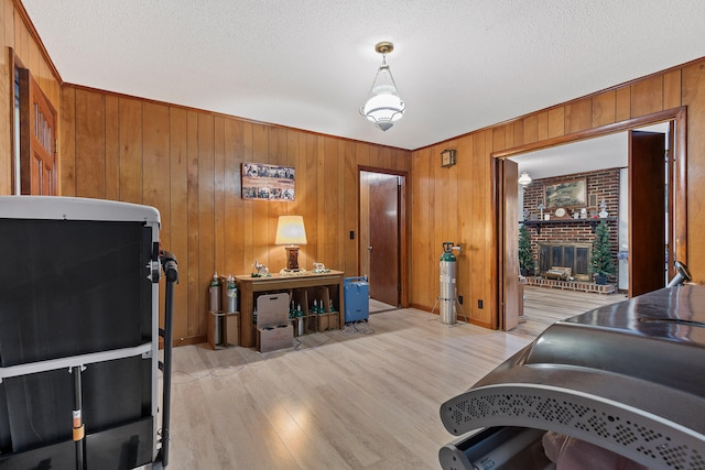 interior space with wood walls, a textured ceiling, light hardwood / wood-style floors, and a brick fireplace