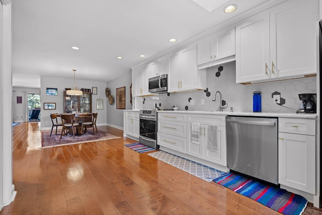 kitchen with white cabinets, tasteful backsplash, hardwood / wood-style flooring, pendant lighting, and stainless steel appliances