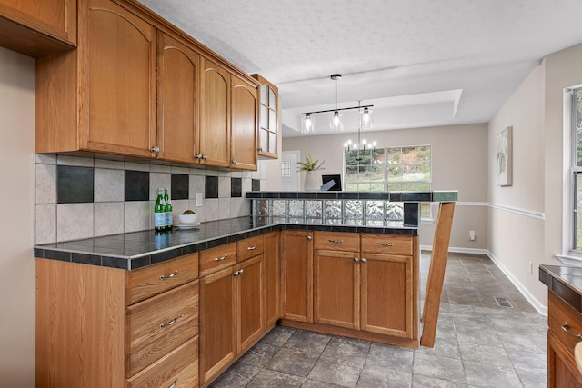 kitchen featuring kitchen peninsula, tasteful backsplash, a textured ceiling, a notable chandelier, and pendant lighting