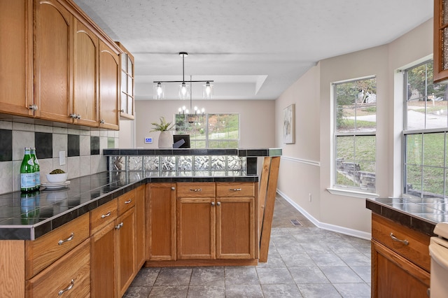 kitchen featuring light tile patterned flooring, kitchen peninsula, a textured ceiling, backsplash, and decorative light fixtures