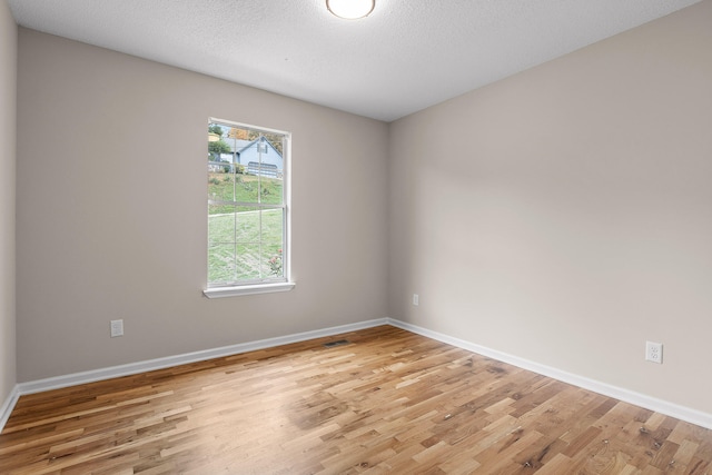 spare room featuring a textured ceiling and light hardwood / wood-style floors