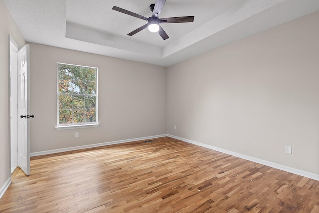 unfurnished room with ceiling fan, a tray ceiling, a textured ceiling, and light hardwood / wood-style floors