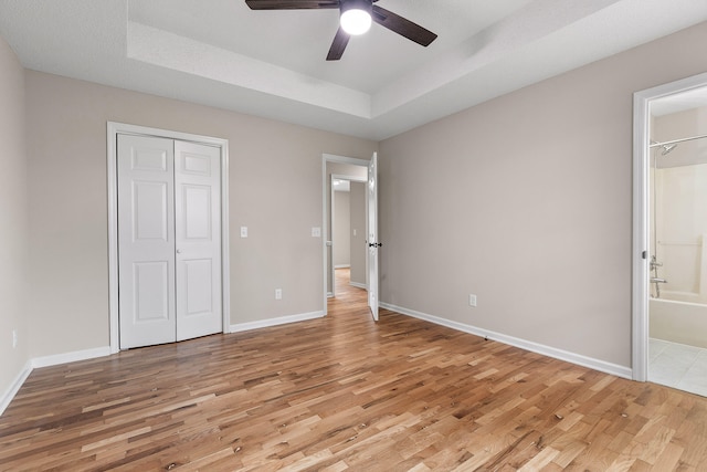 unfurnished bedroom with light wood-type flooring, ensuite bath, ceiling fan, and a closet