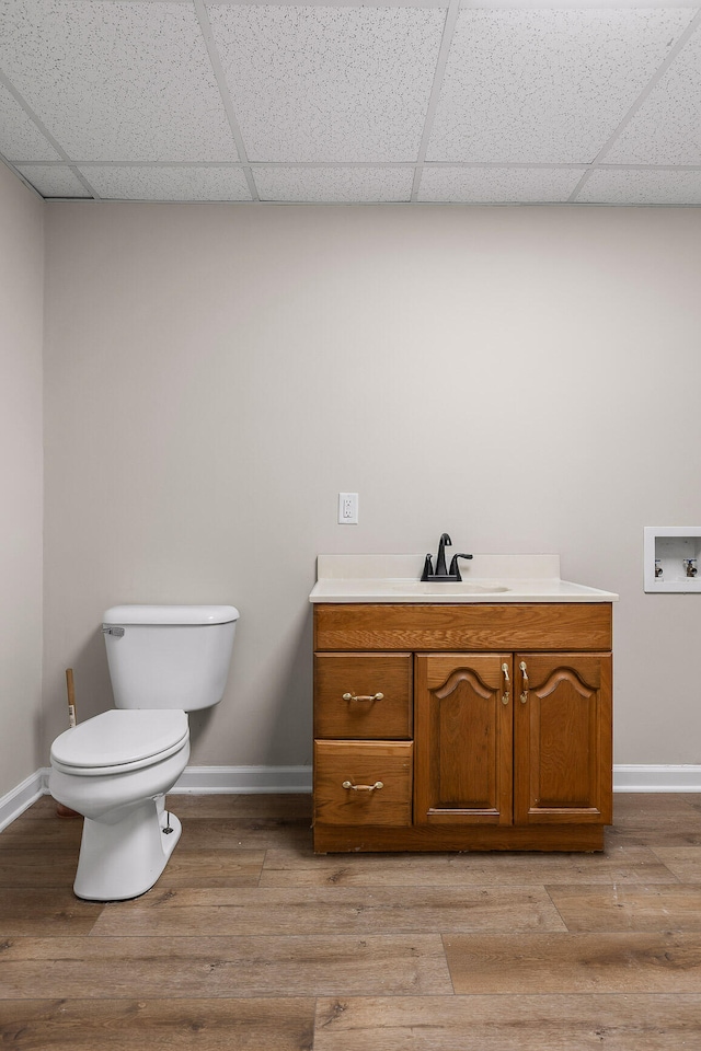 bathroom with wood-type flooring, vanity, toilet, and a drop ceiling