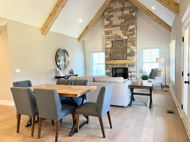 dining area featuring light hardwood / wood-style floors, beam ceiling, a stone fireplace, and high vaulted ceiling