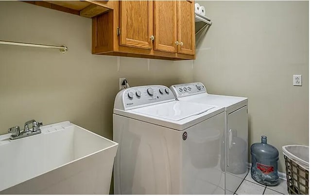 clothes washing area with cabinets, light tile patterned flooring, washing machine and dryer, and sink