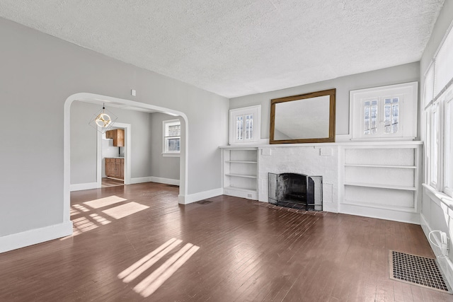 unfurnished living room with dark wood-type flooring, a textured ceiling, a fireplace, and built in shelves