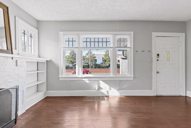 unfurnished living room with dark wood-type flooring, a healthy amount of sunlight, and a textured ceiling