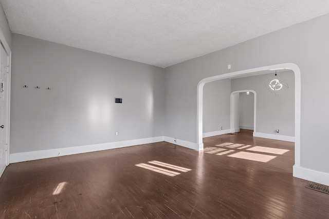 empty room featuring dark wood-type flooring, a textured ceiling, and a chandelier