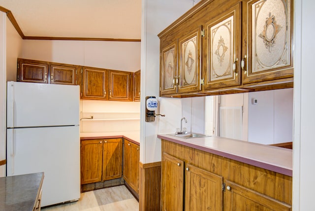 kitchen featuring sink, ornamental molding, light hardwood / wood-style flooring, white fridge, and vaulted ceiling