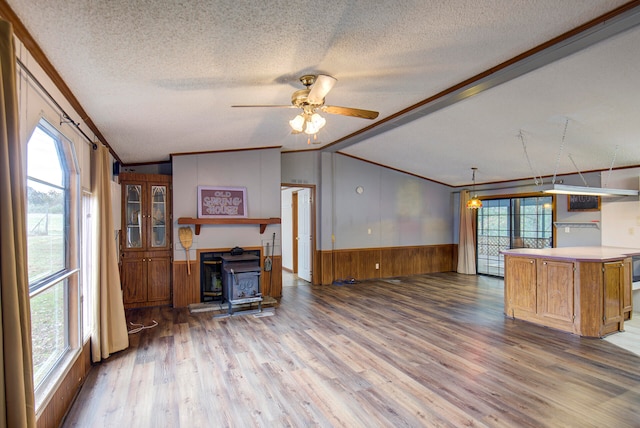 unfurnished living room with a wood stove, wood-type flooring, a textured ceiling, and vaulted ceiling