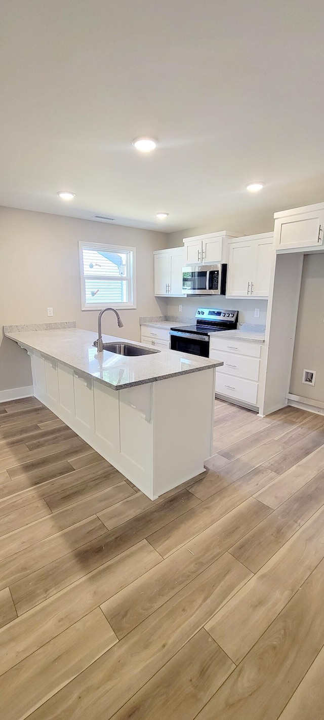 kitchen with appliances with stainless steel finishes, white cabinets, sink, and light hardwood / wood-style floors