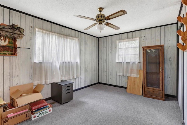 interior space featuring wood walls, ceiling fan, a healthy amount of sunlight, and light carpet