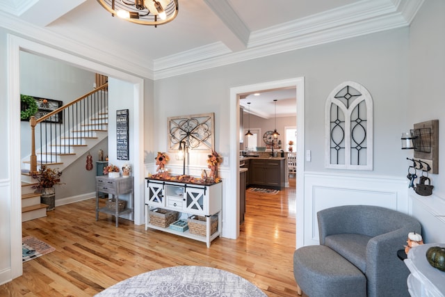 living area featuring wainscoting, light wood-style flooring, stairway, beamed ceiling, and crown molding