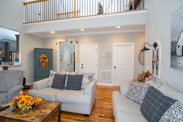 living area with visible vents, a towering ceiling, crown molding, light wood-type flooring, and recessed lighting