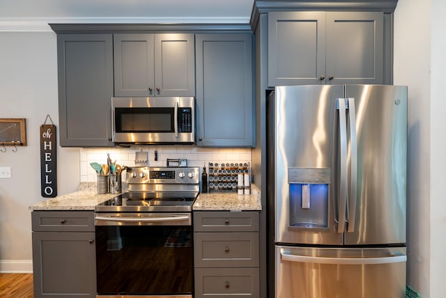 kitchen with stainless steel appliances, gray cabinets, decorative backsplash, and light stone countertops