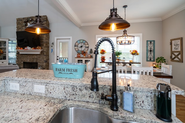 kitchen with wood finished floors, decorative light fixtures, light stone countertops, crown molding, and a fireplace