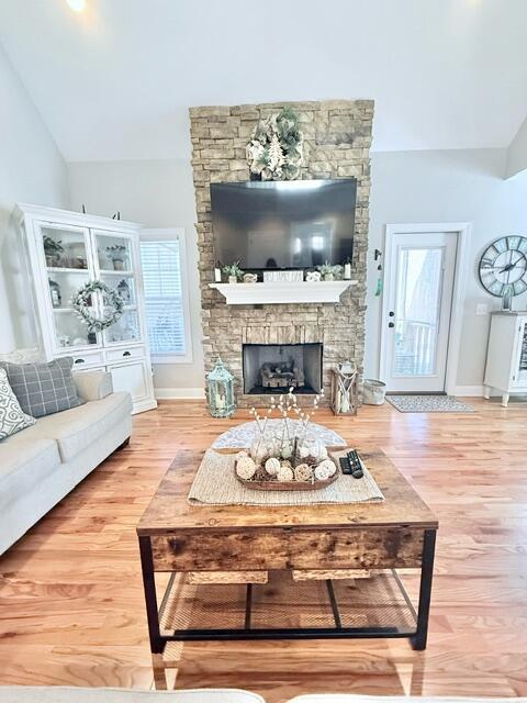 living area featuring lofted ceiling, baseboards, wood finished floors, and a stone fireplace