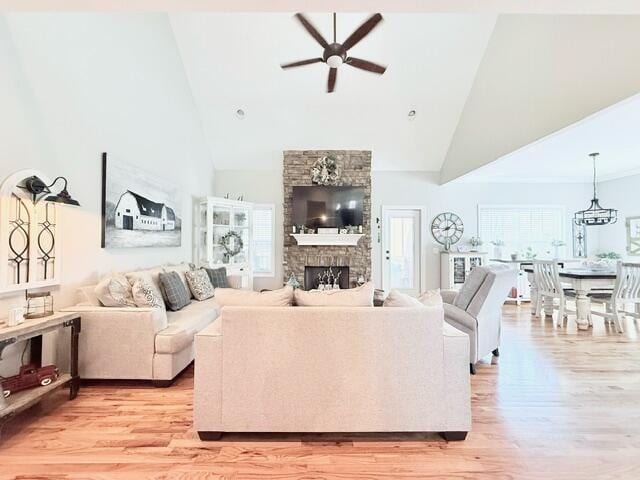 living room with a ceiling fan, light wood-style flooring, a stone fireplace, and high vaulted ceiling