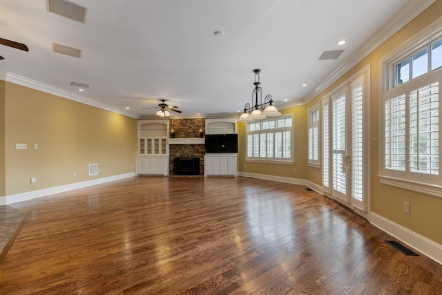 unfurnished living room featuring a stone fireplace, ceiling fan with notable chandelier, dark hardwood / wood-style floors, and crown molding