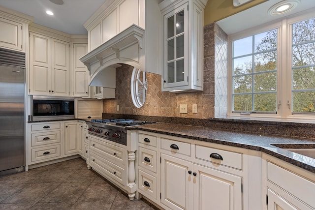 kitchen featuring dark tile patterned flooring, backsplash, built in appliances, and plenty of natural light