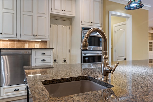 kitchen featuring dark stone counters, white cabinets, ornamental molding, backsplash, and appliances with stainless steel finishes