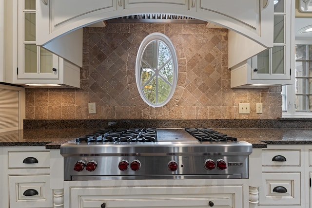 kitchen with dark stone countertops, backsplash, stainless steel gas stovetop, and white cabinets