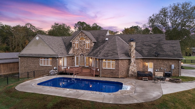 pool at dusk with a wooden deck and a patio