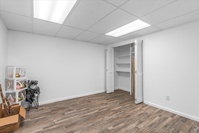 unfurnished bedroom with a drop ceiling, dark wood-type flooring, and a closet