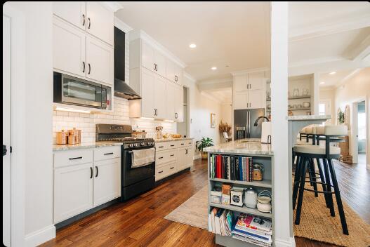 kitchen with dark wood-type flooring, wall chimney exhaust hood, white cabinetry, and appliances with stainless steel finishes