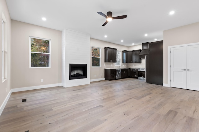 unfurnished living room featuring ceiling fan, a large fireplace, and light hardwood / wood-style flooring