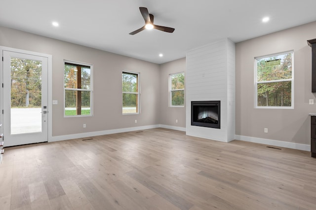 unfurnished living room with ceiling fan, a large fireplace, and light hardwood / wood-style floors