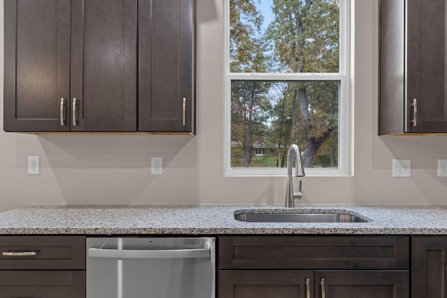 kitchen with dark brown cabinets, light stone counters, stainless steel dishwasher, and sink