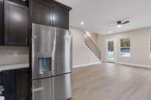 kitchen with light stone countertops, ceiling fan, dark brown cabinets, stainless steel fridge, and light wood-type flooring