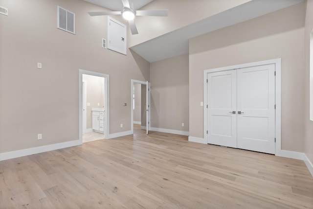 unfurnished bedroom featuring a towering ceiling, ensuite bathroom, ceiling fan, a closet, and light wood-type flooring