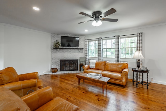 living room with a brick fireplace, wood-type flooring, ceiling fan, and crown molding