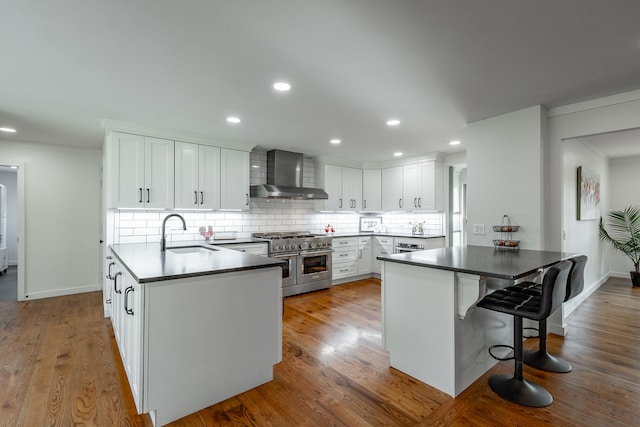 kitchen with light hardwood / wood-style floors, double oven range, wall chimney exhaust hood, sink, and white cabinetry